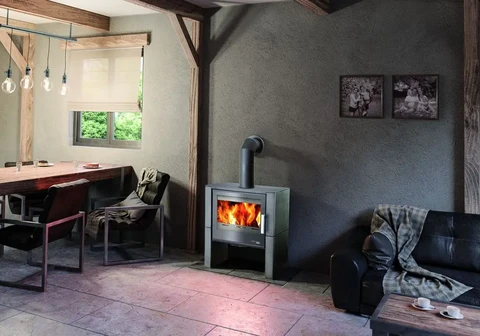 Intérieur moderne avec poêle à bois en fonctionnement, salon cosy avec canapé cuir noir, espace repas avec table bois et chaises design