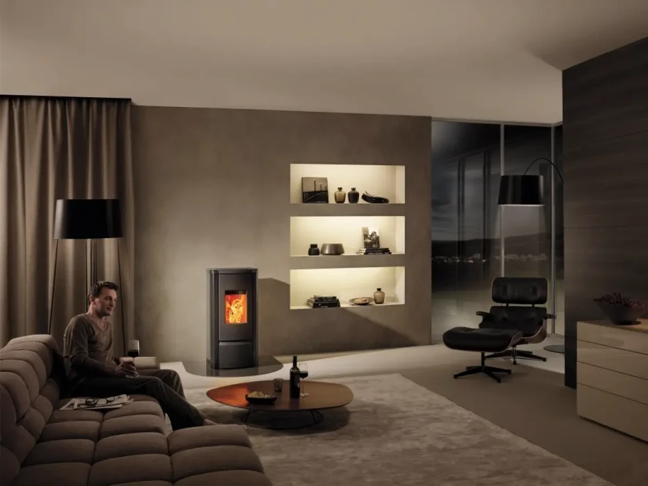 Homme détendu assis dans salon moderne avec poêle à bois en fonctionnement, fauteuil design noir, étagères murales éclairées, rideaux beiges et mobilier contemporain